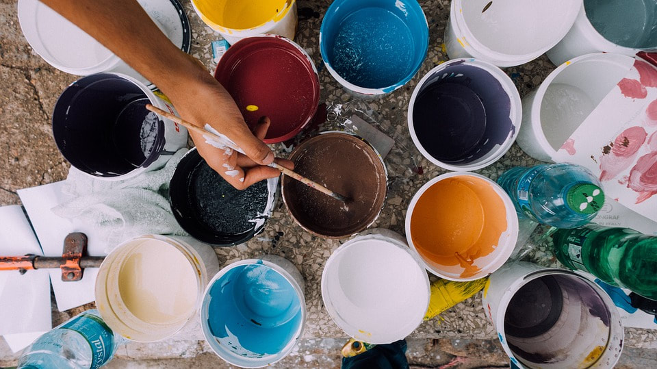 Different colors in paint buckets from above view showing person's arm dipping brush.